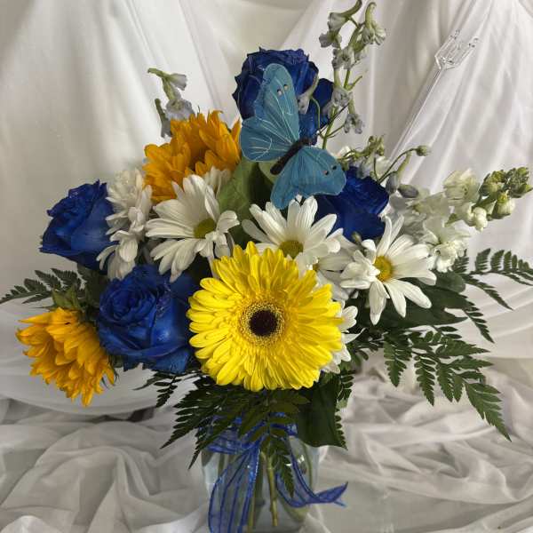 Bouquet of blue roses, white daisies, and yellow gerbera daisies in a glass vase