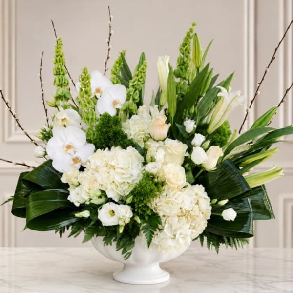 White floral arrangement in a white pedestal vase with orchids and lilies