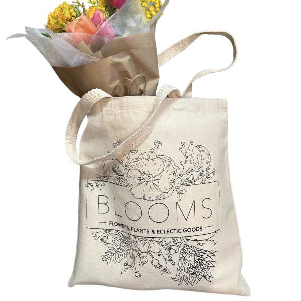 Small bouquet of pink and yellow flowers in brown paper, tucked into a canvas tote bag