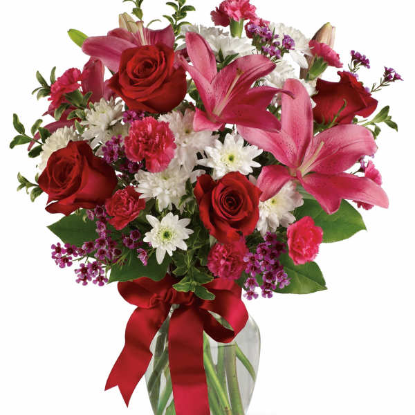 Bouquet of red roses, pink lilies, and white daisies in a glass vase with a red ribbon
