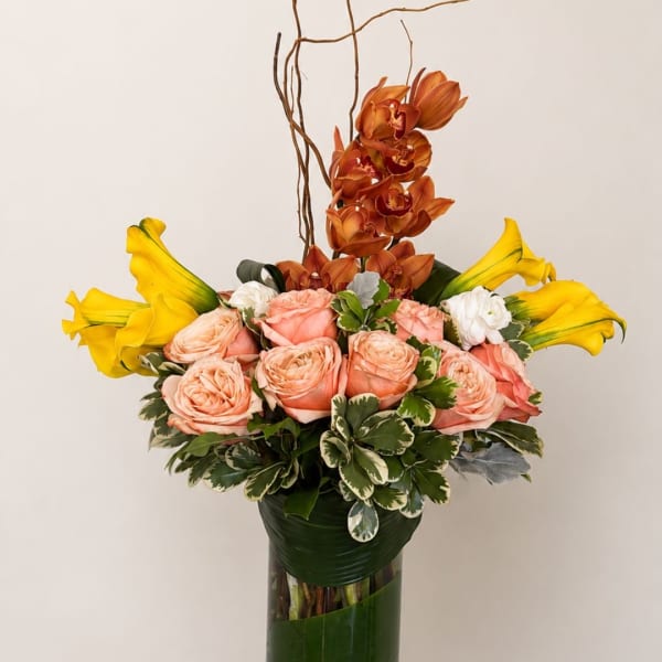 Bouquet of peach roses, yellow calla lilies, and orange orchids in a tall vase