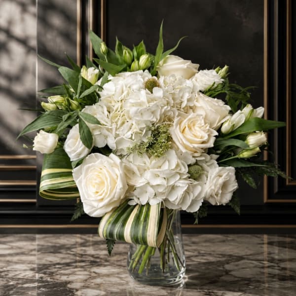 White roses and hydrangeas in a clear glass vase with striped leaf wrap