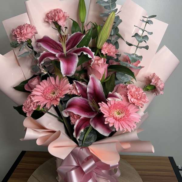 Pink lily and gerbera bouquet wrapped in blush paper with a satin ribbon