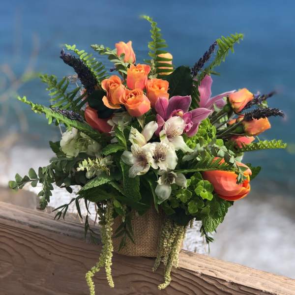 Mixed bouquet with orange roses and purple orchids in a burlap-wrapped container