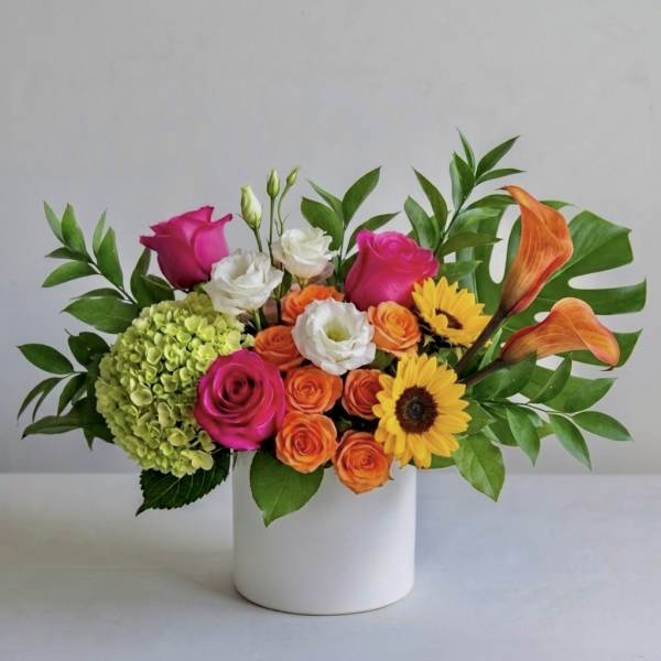 Mixed bouquet in a white vase with roses, hydrangea, calla lilies, and sunflowers