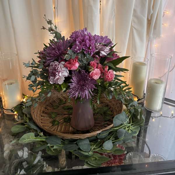 Purple and pink floral arrangement in a mauve vase with candles nearby