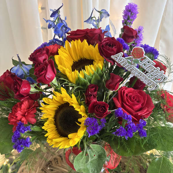 Basket arrangement with red roses, sunflowers, and purple flowers