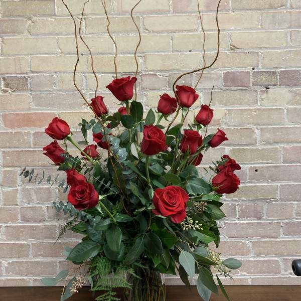 Tall bouquet of red roses in a glass vase with curly branches