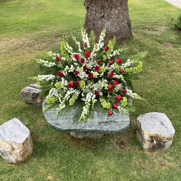 Large red and white floral arrangement on a stone bench outdoors