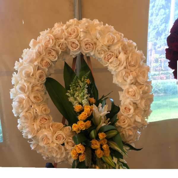 Large circular floral wreath of cream roses with yellow blooms at the base