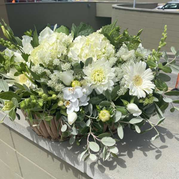 White floral arrangement in a woven basket with mixed greenery