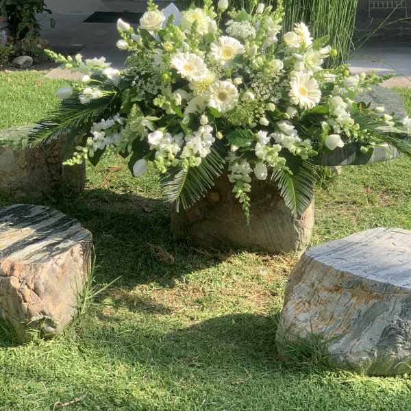 Large white floral arrangement with daisies and roses in an outdoor setting