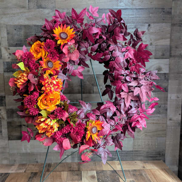 Circular wreath with orange and magenta flowers on a metal stand