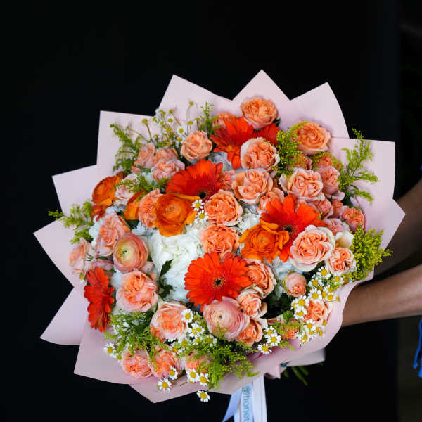Bouquet of peach roses and orange gerbera daisies wrapped in pink paper