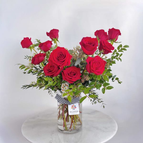 Red roses arranged in a clear glass vase with greenery