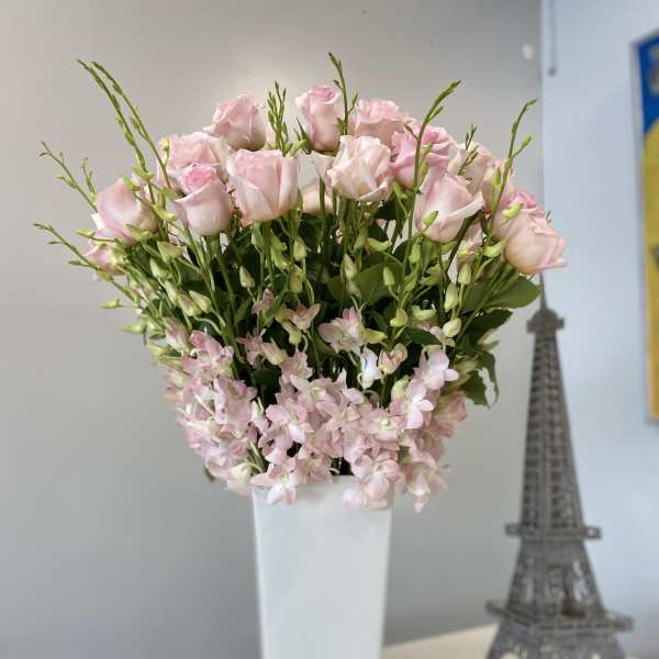Pink roses and small pale pink flowers in a tall white vase