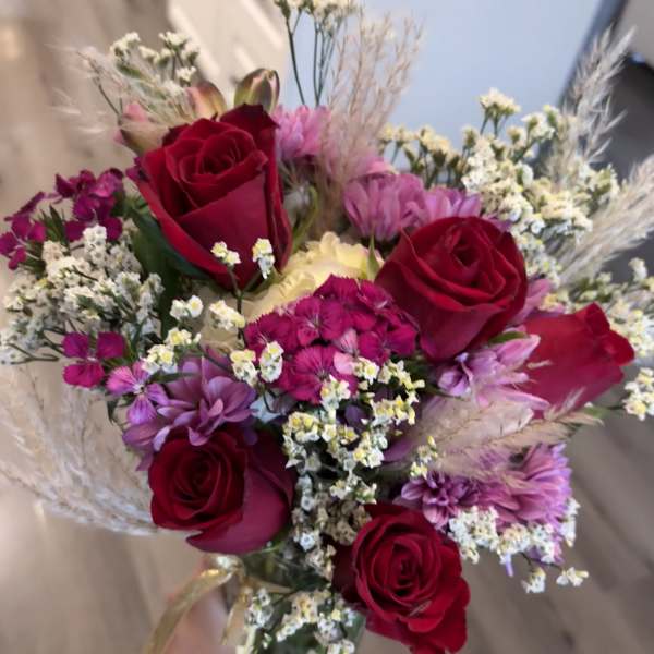Handheld bouquet of red roses and pink-purple flowers in a clear vase