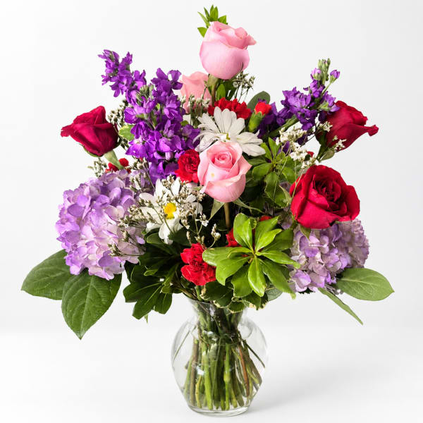 Mixed bouquet of roses, hydrangeas, and daisies in a clear glass vase