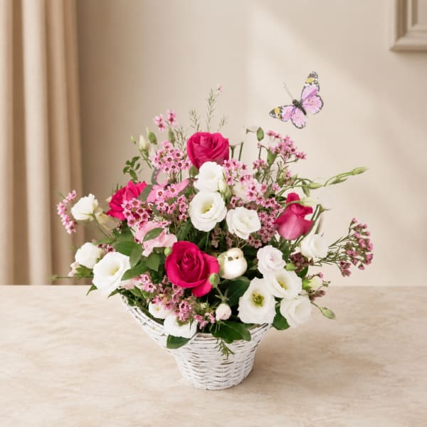 Pink and white flower arrangement in a white basket with a butterfly accent