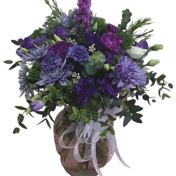 Purple floral arrangement in a round glass vase with a ribbon bow