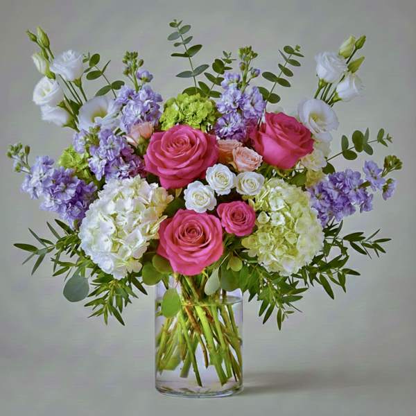 Pink and white roses with lavender blooms in a clear glass vase