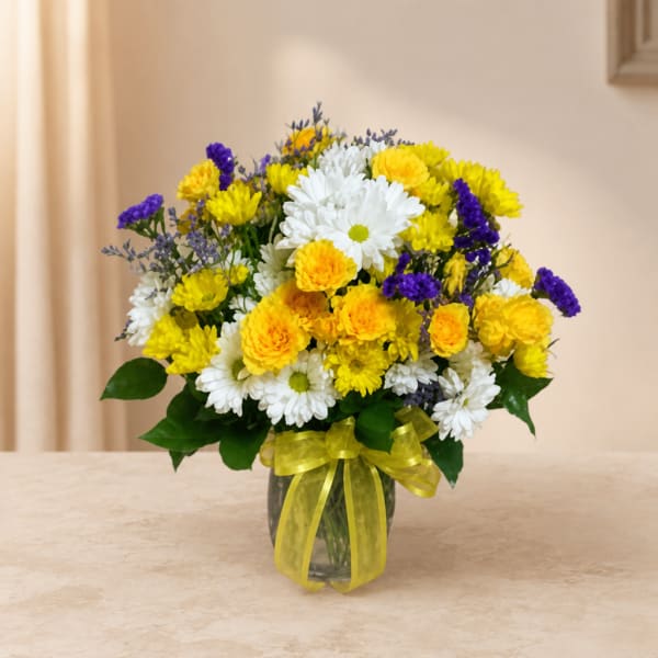 Bouquet of yellow, white, and purple flowers in a glass vase with a yellow ribbon