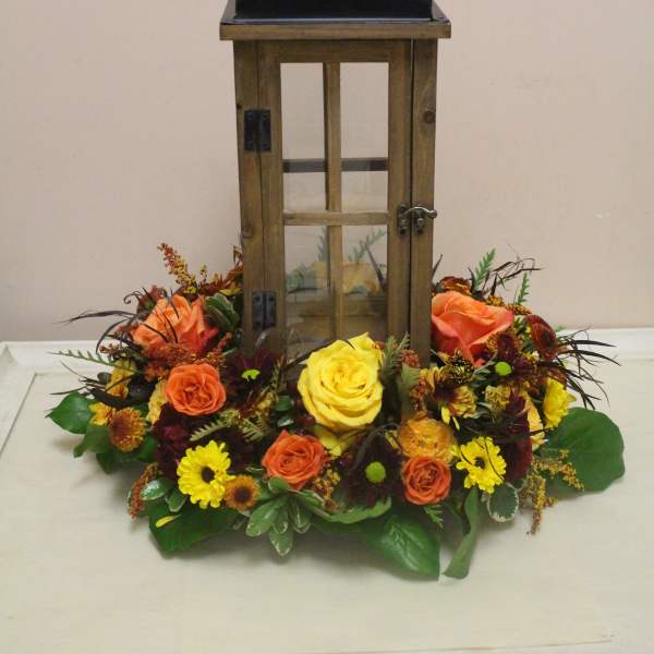 Lantern centerpiece surrounded by orange, yellow, and burgundy flowers
