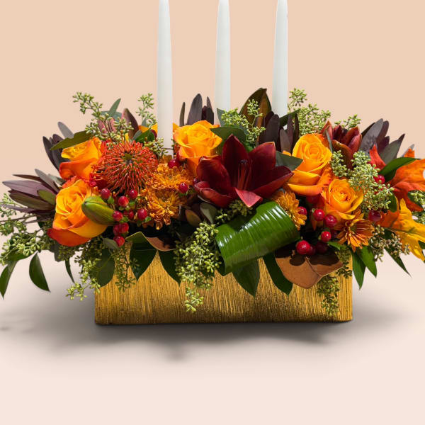 Orange and burgundy floral centerpiece with three white taper candles