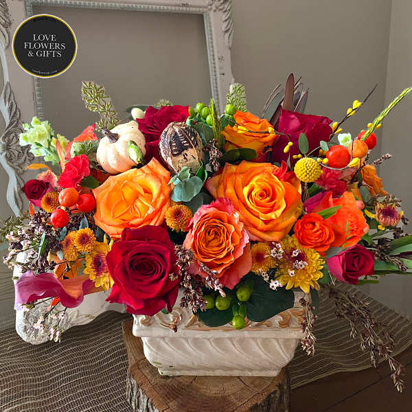 Low arrangement of orange and red roses with yellow accents in a white rectangular vase