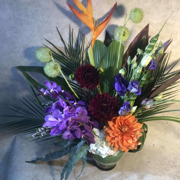 Tropical floral arrangement with purple orchids and orange blooms in a vase