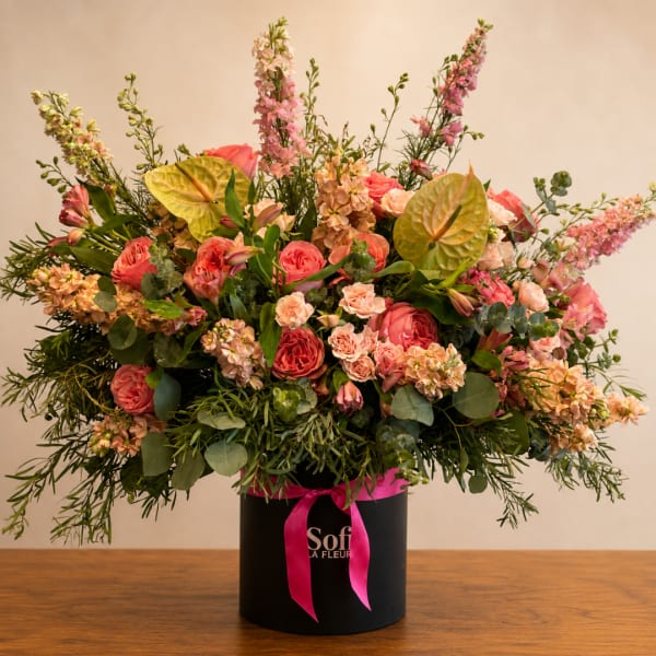Large pink and peach floral arrangement in a black hatbox with a ribbon