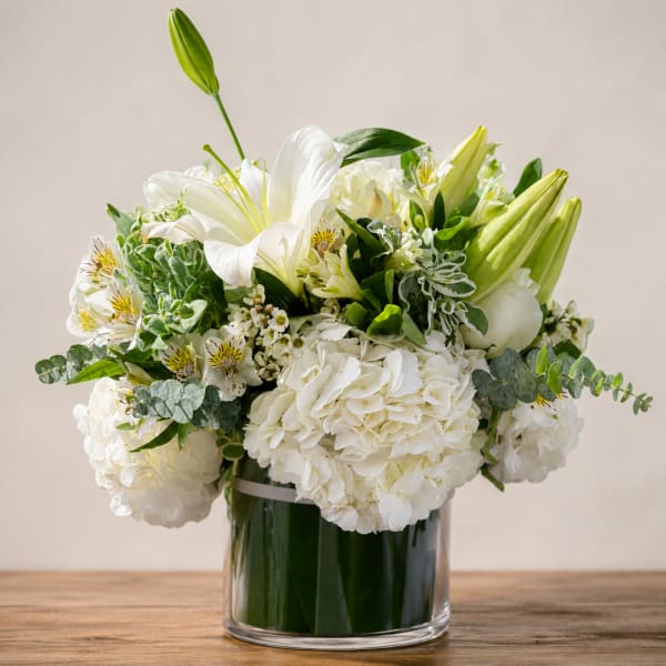 White lilies and hydrangeas in a glass vase with mixed greenery