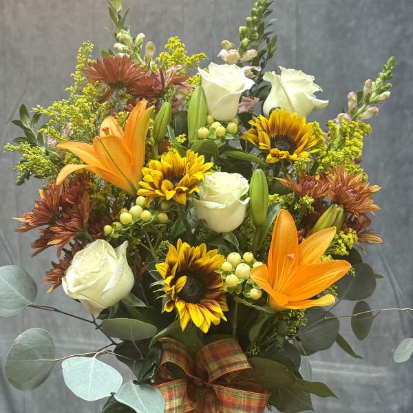Mixed bouquet with white roses, sunflowers, orange lilies, and a plaid ribbon in a glass vase