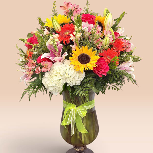 Mixed bouquet of roses, lilies, sunflowers, and gerbera daisies in a glass vase