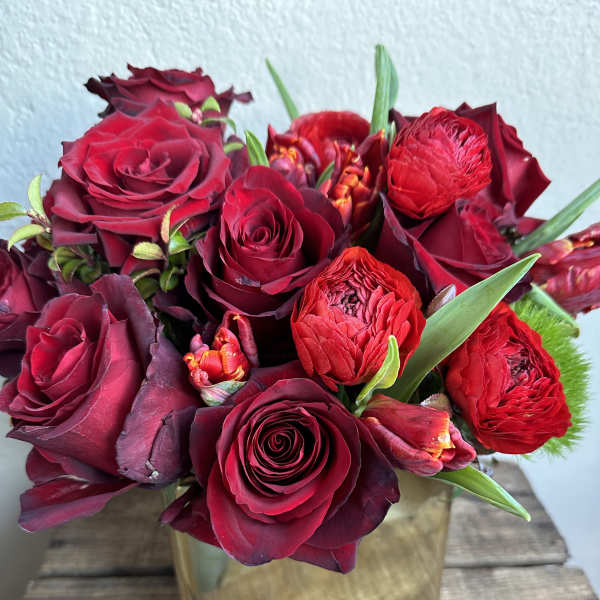 Red roses and ranunculus arranged in a square gold vase
