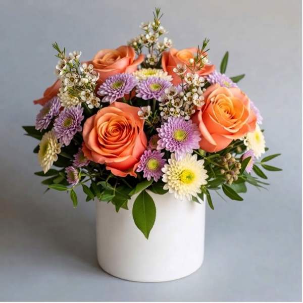 Bouquet of peach roses and purple daisies in a white vase