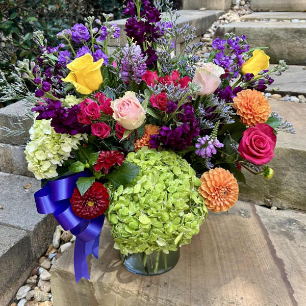 Colorful mixed flower arrangement in a glass vase with roses, hydrangeas, and dahlias
