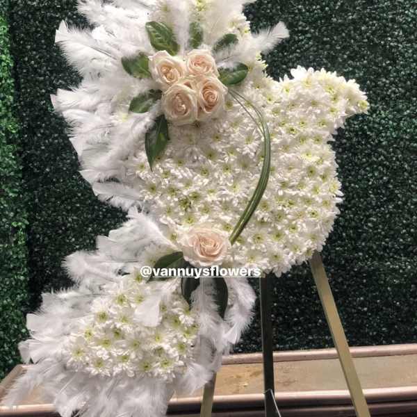 Angel-shaped standing spray of white flowers with blush roses and feathers on a metal easel