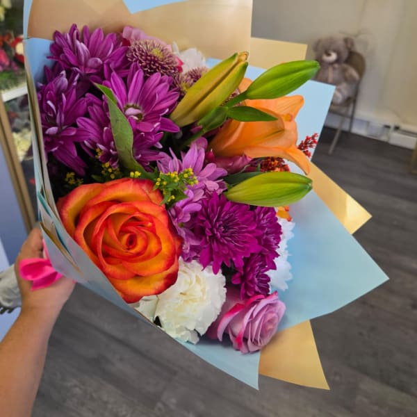 Bouquet of purple chrysanthemums, orange lilies, and roses wrapped in blue paper