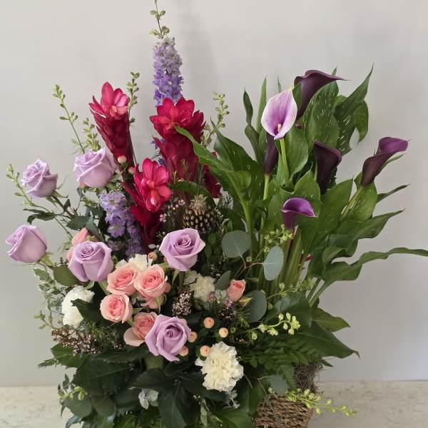 Mixed bouquet with roses, calla lilies, and purple flowers in a woven basket