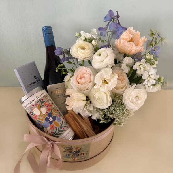 Flower arrangement in a round gift box with wine and tea tins