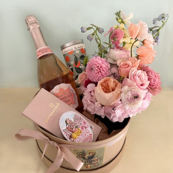 Pink floral gift box with a rose bouquet, champagne bottle, and candy tin