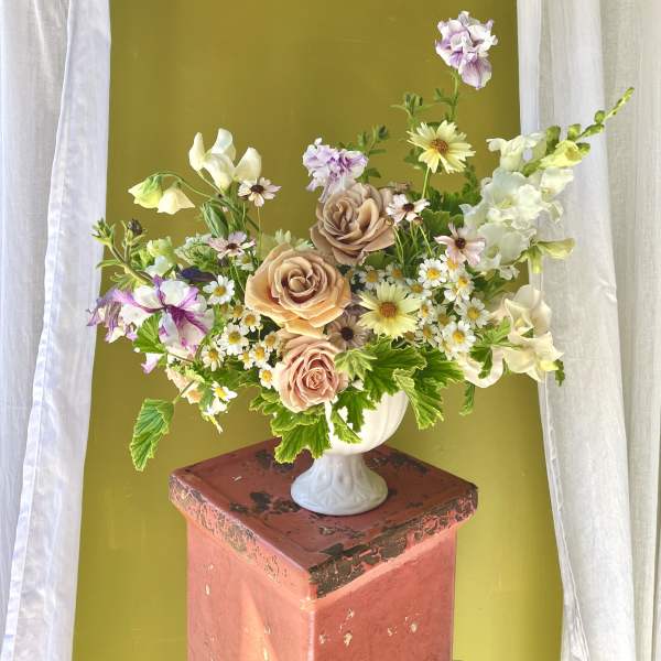 Mixed bouquet of peach roses and small white daisies in a white vase