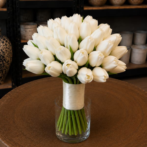 White tulip bouquet in a clear glass vase with ribbon wrap