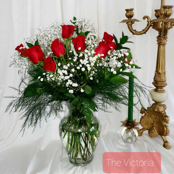 Red roses and baby's breath in a clear glass vase beside a gold candlestick