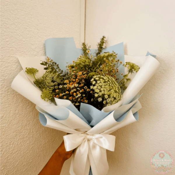 Handheld bouquet of white and green flowers wrapped in blue and white paper
