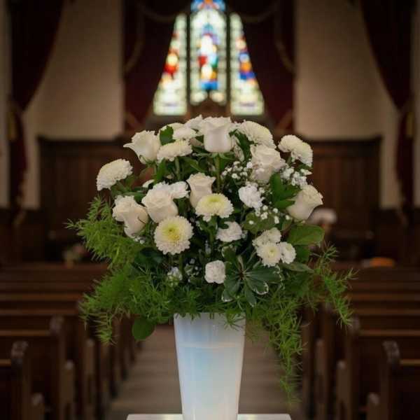 White floral arrangement in a tall glass vase on a pedestal