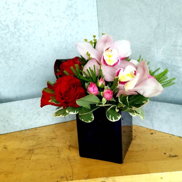 Red roses and pale pink orchids in a black square vase