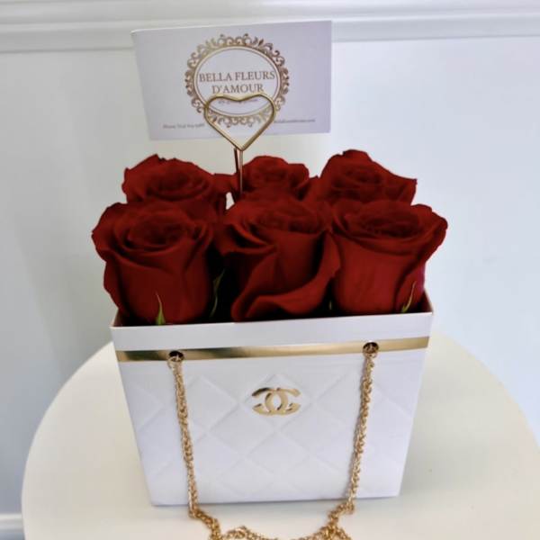 Red roses arranged in a white gift box with a gold chain handle