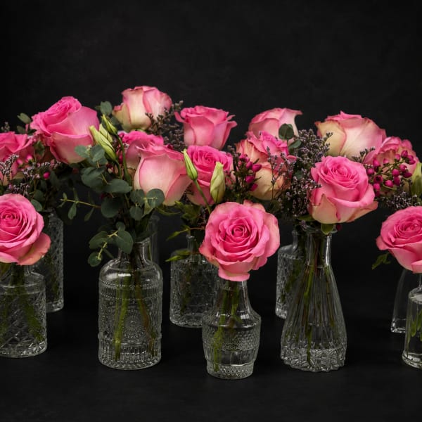 Pink roses arranged in small clear glass vases with greenery